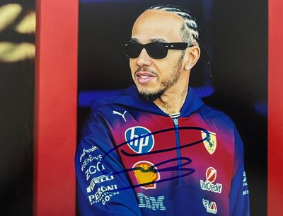 photo dédicacée d'un homme vêtu d'une veste bleue et portant des lunettes de soleil, devant un cadre rouge