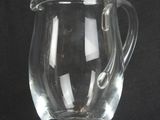 a clear glass pitcher with a handle on a black background
