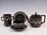 three pieces of black and gold decorated tea set on a white surface