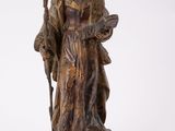 une vieille statue représentant un homme tenant un bâton, posée sur un socle en bois