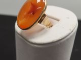 une bague en pierre orange posée sur un socle blanc