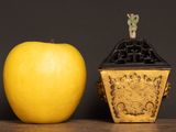 a yellow apple next to a golden vase on a table
