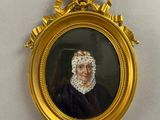 portrait d'une femme en robe noire, dans un cadre doré, accroché à un mur blanc