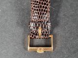 a close up of a watch on a black surface with a gold buckle