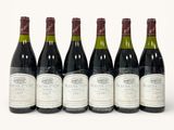 six bottles of wine are lined up in a row on a white surface