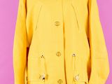 un manteau jaune posé sur un mannequin, devant un fond rose