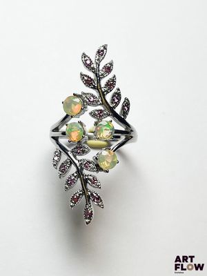 un gros plan d'une bague posée sur une surface blanche, entourée de fleurs et de feuilles