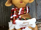 une statue représentant un chien coiffé d'un bonnet de Père Noël et tenant une pancarte