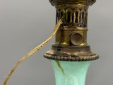 a green glass lamp with a gold handle on a table