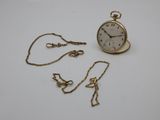 a small gold pocket watch and chain on a white surface