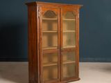 une vieille armoire en bois avec des portes vitrées, devant laquelle se trouve une chaise