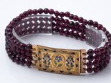 un gros plan sur un bracelet composé de perles rouges et muni d'un fermoir doré