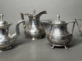 three silver teapots and a coffee pot on a table