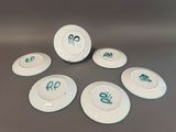 six white plates with green writing on them sitting on top of a table