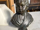un buste en bronze représentant un garçon, posé sur une table à côté d'un cadre photo
