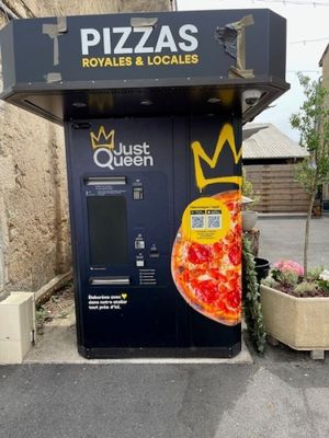 un distributeur automatique sur lequel est posée une pizza, devant un immeuble