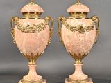 paire d'urnes anciennes en marbre rose rehaussées de touches dorées, posées sur des socles