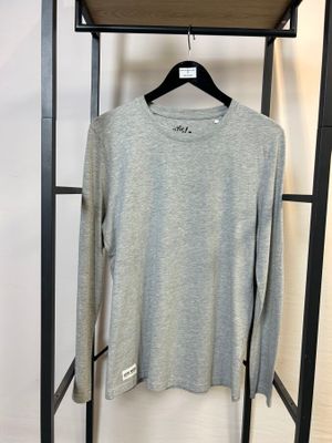 un t-shirt gris à manches longues suspendu à un porte-vêtements dans une pièce