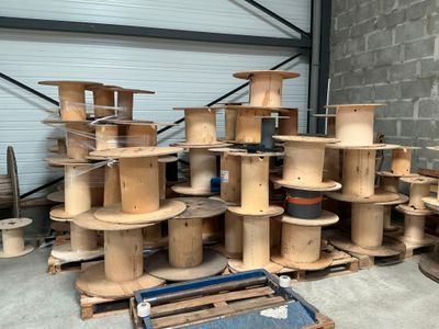 Plusieurs bobines en bois sont empilées sur des palettes dans un entrepôt