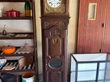 a grandfather clock in the corner of a room next to a shelf with pots and pans on it