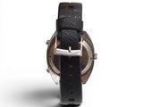 the back of a watch with a black leather band and a silver buckle