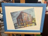 painting of a building on a easel with a blue frame