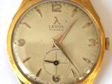 une montre-bracelet en or posée sur une surface blanche
