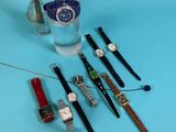 several different watches and a vase of flowers on a blue surface