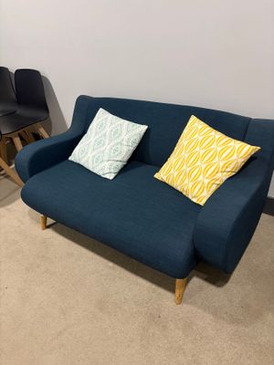 a blue couch with two pillows on it in the corner of a room