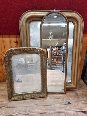 trois miroirs posés sur une table, avec un mur rouge en arrière-plan