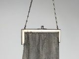 a silver mesh purse hanging from a chain on a gray background
