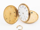 a gold pocket watch and a gold ring on a white surface