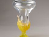 a glass vase with a yellow flower inside of it on a white surface