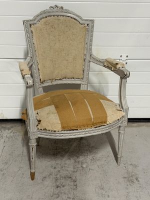 Une vieille chaise dont l'assise est abîmée est posée devant la porte d'un garage.