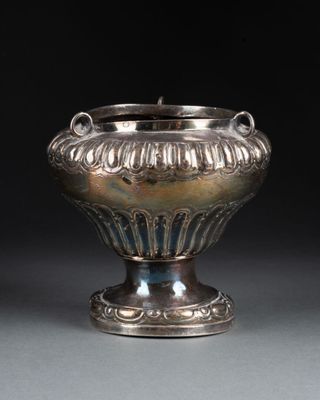 un vase ancien en argent posé sur une table, devant un fond noir