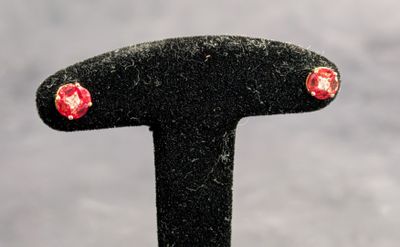 une paire de boucles d'oreilles à clous ornées de fleurs rouges et blanches, posées sur un socle noir