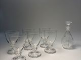 six verres à vin et une carafe posés sur un plan de travail blanc