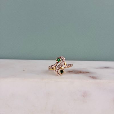 une photo d'une bague sertie d'un diamant et d'une émeraude posée sur une surface en marbre