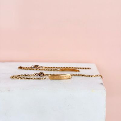 a gold plated bracelet on a marble block with a pink background