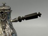 a silver tea pot with a handle on a stand