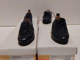 deux paires de chaussures noires posées sur des cartons, sur une surface blanche