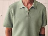 a man standing in front of a white wall wearing a green shirt and white pants
