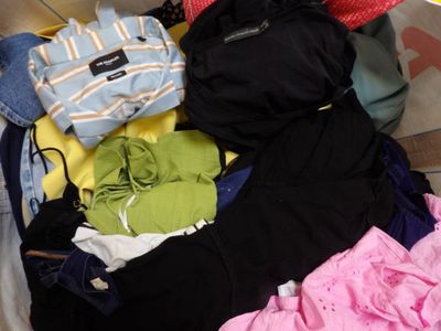une valise pleine de vêtements et des vêtements posés par terre