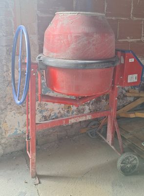 a red cement mixer sitting in front of a brick wall
