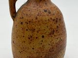a brown vase with a handle sitting on a white surface