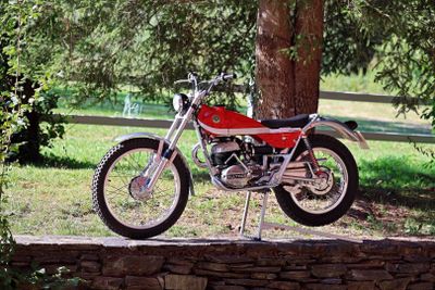 a red motorcycle parked on a stone wall by a tree