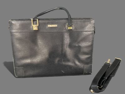 black leather briefcase with gold hardware and strap on grey background