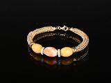 un bracelet plaqué or orné de perles orange et blanches sur un fond noir