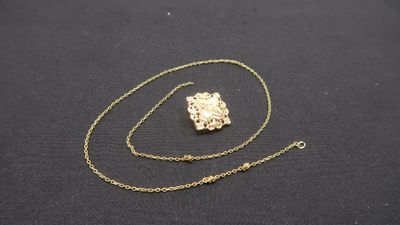 a gold necklace with a chain that has a small piece of gold on it