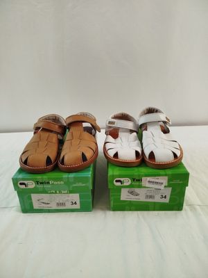 Deux paires de sandales sont posées sur des cartons, sur un lit.